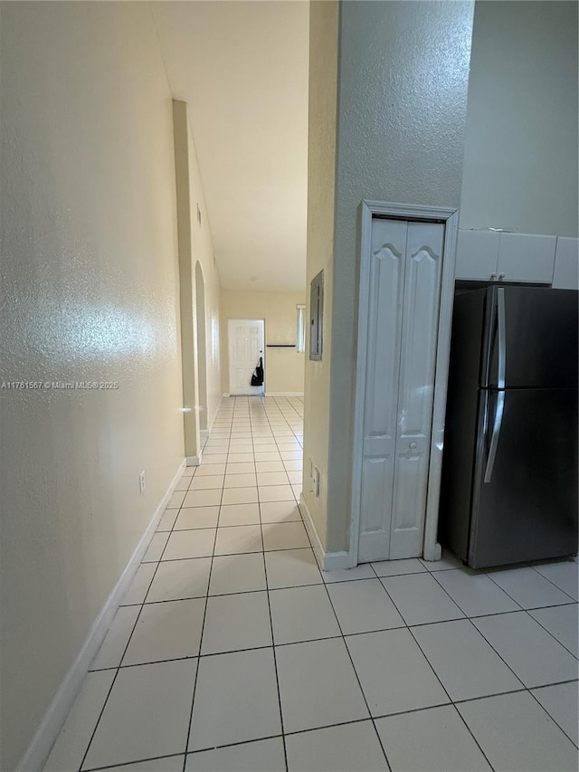 hallway featuring light tile patterned floors, baseboards, and arched walkways