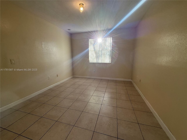 unfurnished room with light tile patterned floors, a textured wall, and baseboards