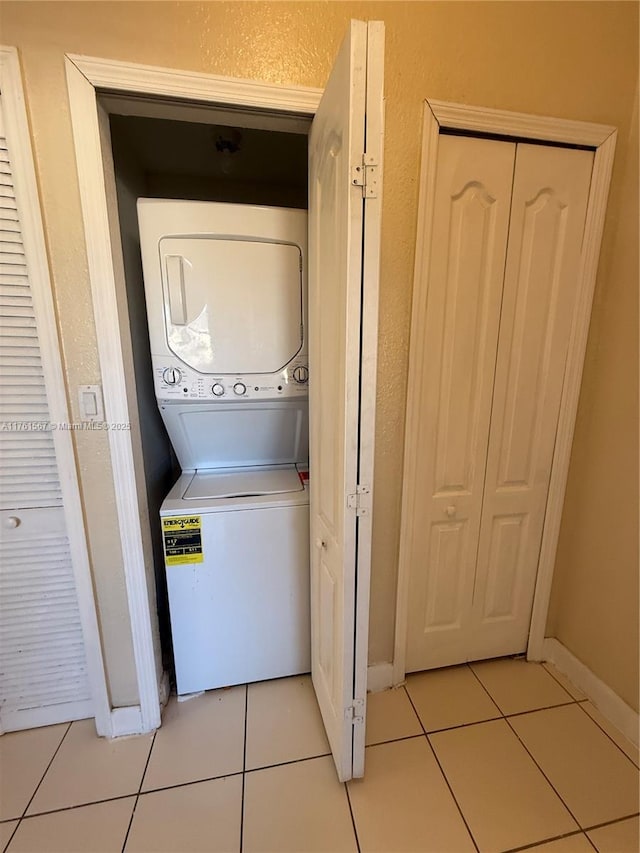 clothes washing area featuring light tile patterned floors, stacked washer / drying machine, laundry area, and a textured wall