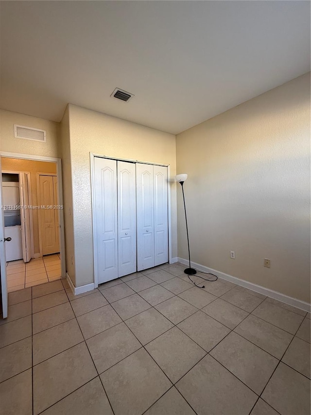 unfurnished bedroom with light tile patterned floors, visible vents, a closet, and baseboards