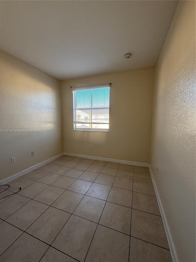 unfurnished room featuring light tile patterned flooring, a textured wall, and baseboards