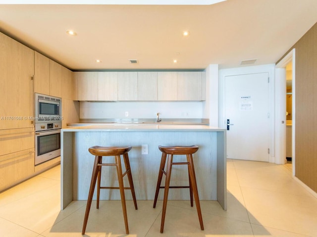 kitchen featuring light brown cabinets, a kitchen breakfast bar, appliances with stainless steel finishes, light tile patterned flooring, and light countertops