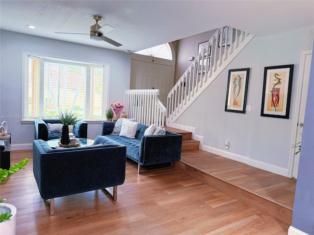 living room with a textured ceiling, stairway, light wood-style floors, baseboards, and ceiling fan