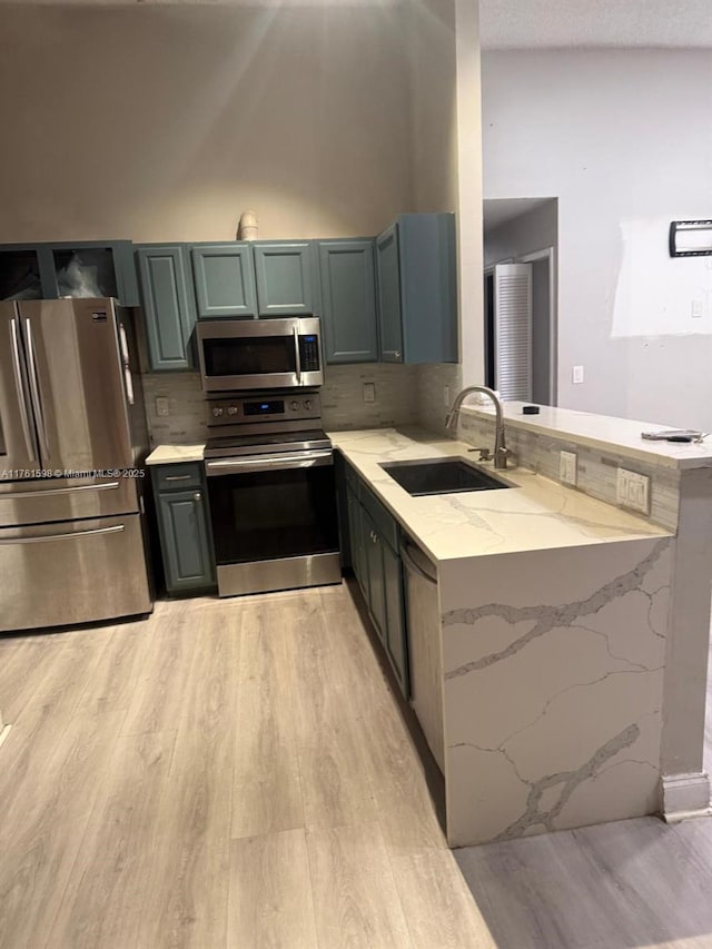 kitchen with light stone countertops, stainless steel appliances, light wood-style floors, and a sink