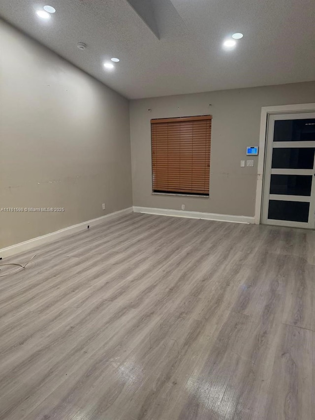 empty room featuring recessed lighting, baseboards, a textured ceiling, and light wood-style flooring