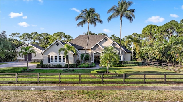 view of front of property featuring driveway, stucco siding, a front lawn, stone siding, and a fenced front yard