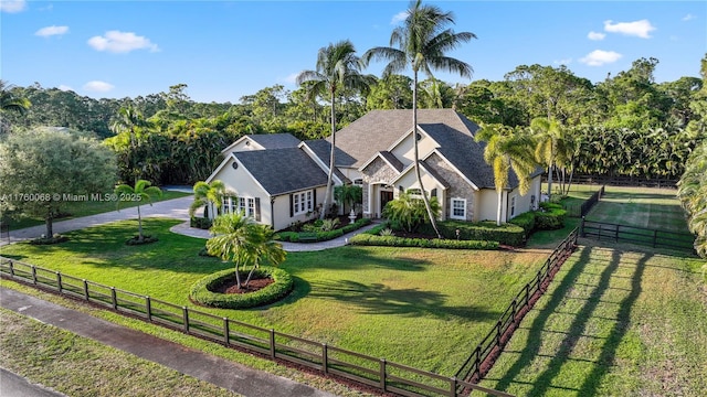 view of front of house with stucco siding, a shingled roof, a front yard, and fence