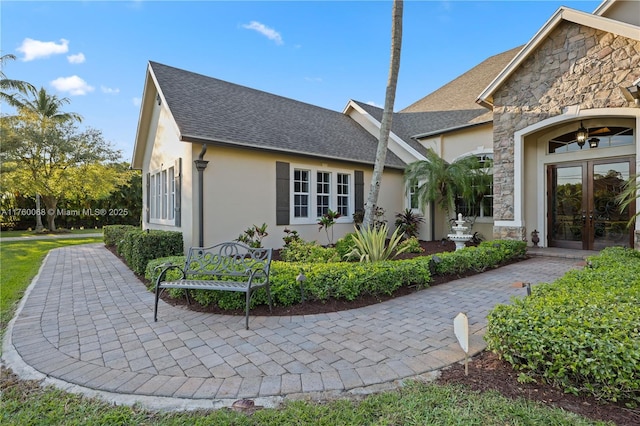 view of front facade featuring stone siding, stucco siding, french doors, and a shingled roof