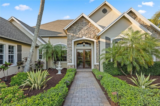 property entrance with french doors, stone siding, roof with shingles, and stucco siding