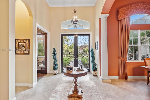 entryway featuring baseboards, ornamental molding, light tile patterned floors, a high ceiling, and ornate columns