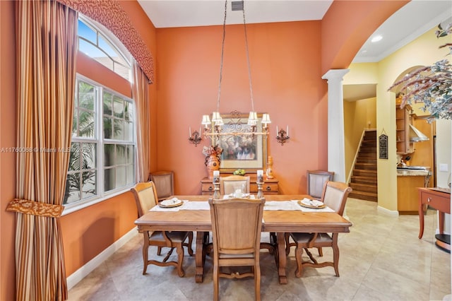 dining space featuring arched walkways, decorative columns, baseboards, a towering ceiling, and stairs