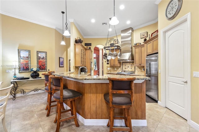 kitchen featuring wall chimney range hood, light stone counters, a peninsula, arched walkways, and stainless steel appliances