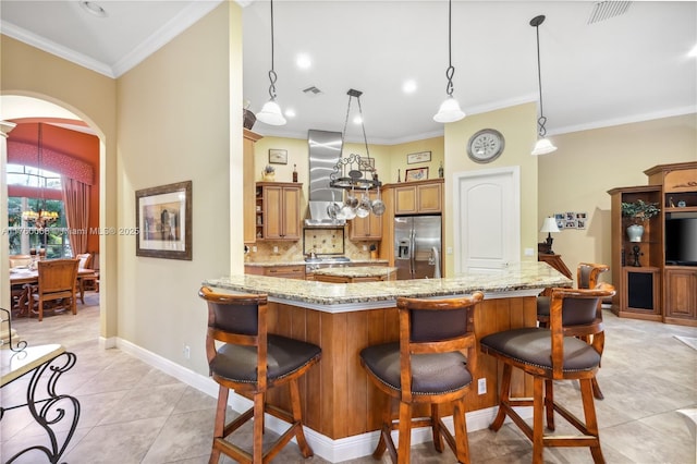 kitchen featuring visible vents, stainless steel fridge, arched walkways, wall chimney exhaust hood, and decorative backsplash