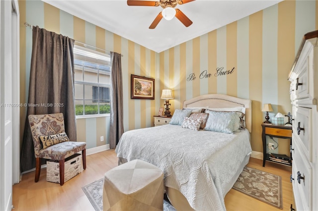 bedroom with light wood finished floors, wallpapered walls, baseboards, and a ceiling fan