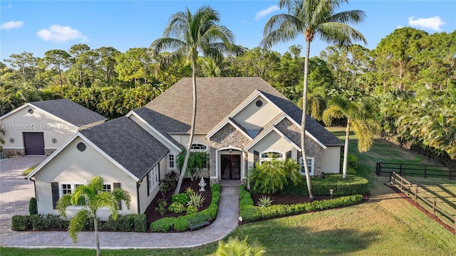 view of front of property featuring a front lawn, fence, stone siding, and a shingled roof