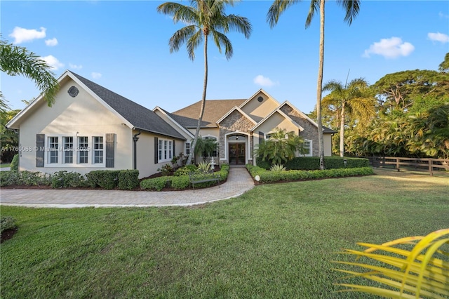 view of front facade with a front lawn, fence, stone siding, and stucco siding