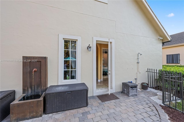 view of exterior entry with a patio area, stucco siding, and fence