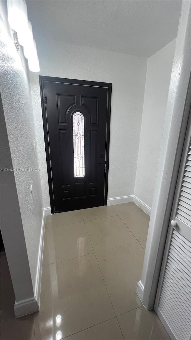 tiled entryway with a textured wall and baseboards