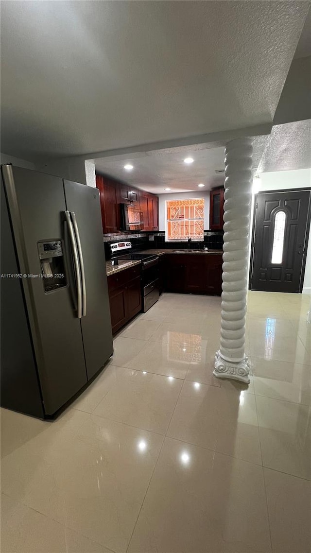 kitchen featuring ornate columns, light tile patterned flooring, appliances with stainless steel finishes, dark countertops, and reddish brown cabinets