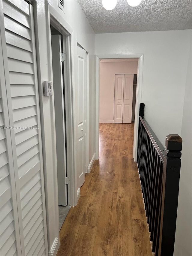 corridor with baseboards, wood finished floors, visible vents, and a textured ceiling