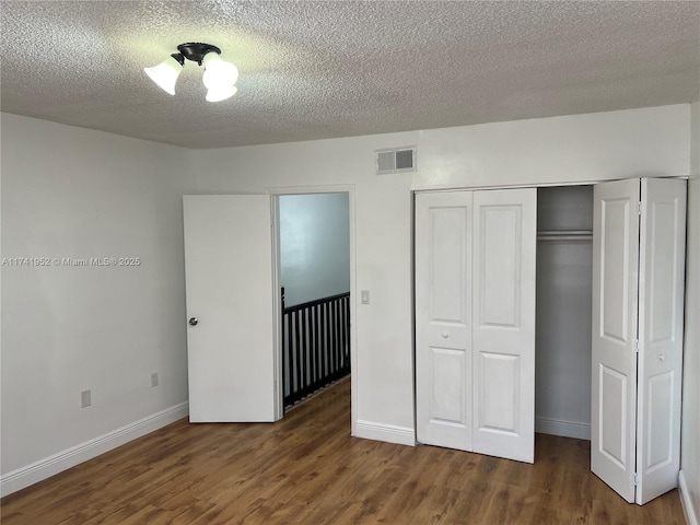 unfurnished bedroom featuring visible vents, baseboards, wood finished floors, a closet, and a textured ceiling