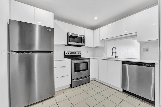 kitchen with light countertops, decorative backsplash, white cabinets, stainless steel appliances, and a sink