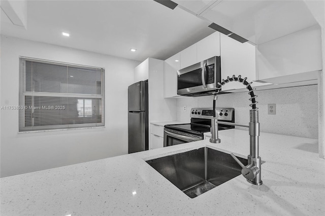 kitchen with modern cabinets, light stone counters, a sink, white cabinetry, and appliances with stainless steel finishes