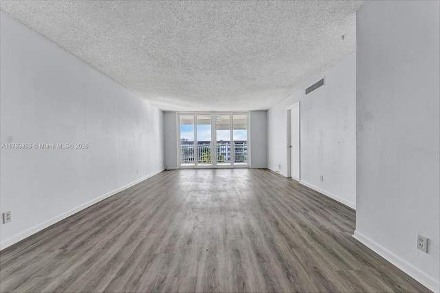 unfurnished room with visible vents, baseboards, floor to ceiling windows, wood finished floors, and a textured ceiling