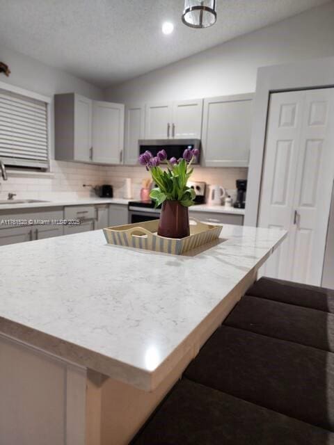 kitchen with a kitchen island, light countertops, vaulted ceiling, appliances with stainless steel finishes, and a sink