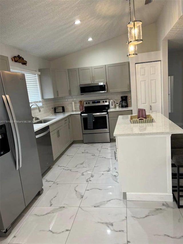 kitchen with gray cabinetry, a sink, backsplash, stainless steel appliances, and vaulted ceiling