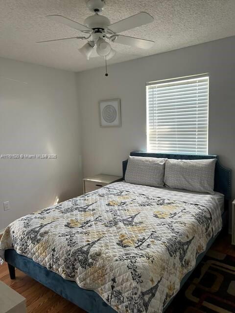 bedroom with a textured ceiling, a ceiling fan, and wood finished floors