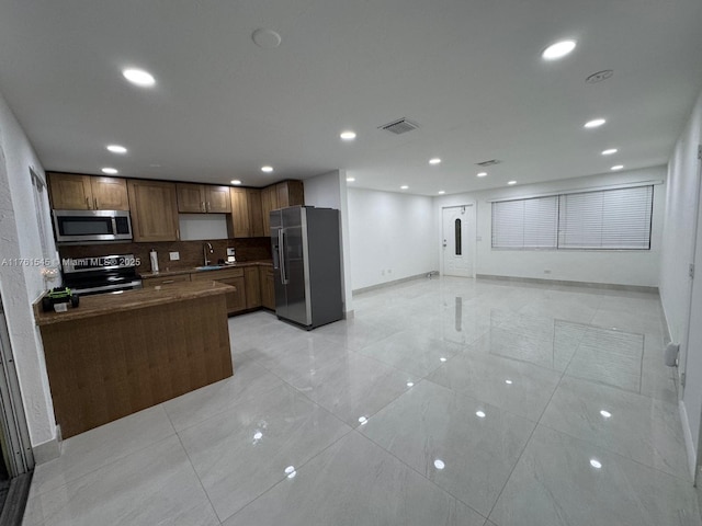 kitchen with visible vents, a sink, backsplash, open floor plan, and stainless steel appliances