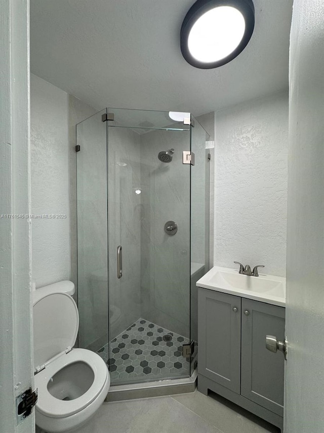 full bathroom with a shower stall, toilet, a textured wall, tile patterned floors, and vanity