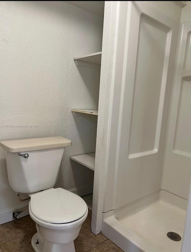 full bathroom with tile patterned floors, toilet, a shower stall, baseboards, and a textured wall