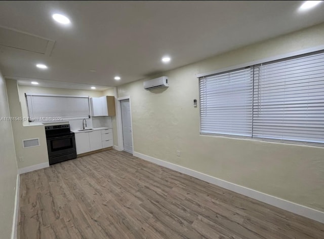 kitchen with visible vents, light wood-style flooring, an AC wall unit, white cabinets, and black range with electric cooktop