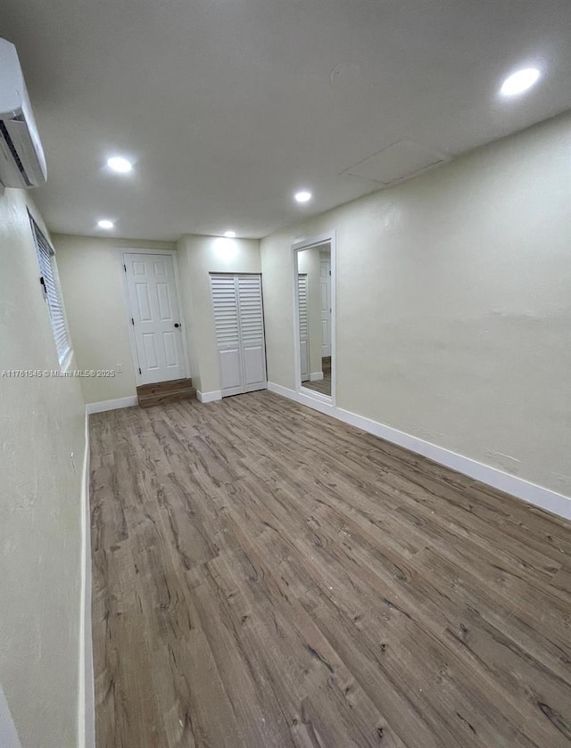 below grade area with recessed lighting, wood finished floors, baseboards, and a wall mounted AC