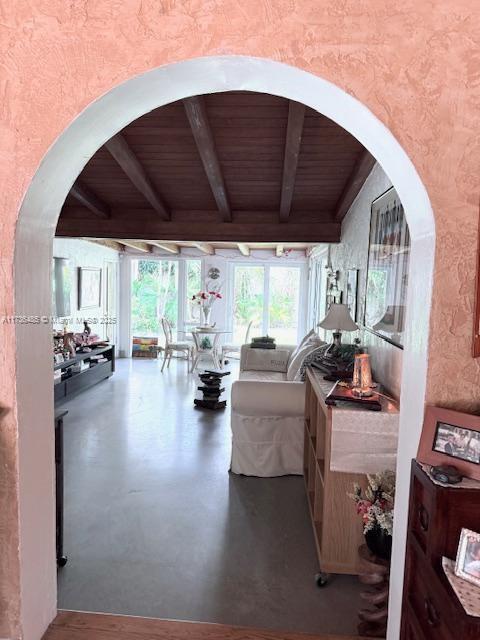 living area with wood ceiling, beamed ceiling, arched walkways, and concrete flooring