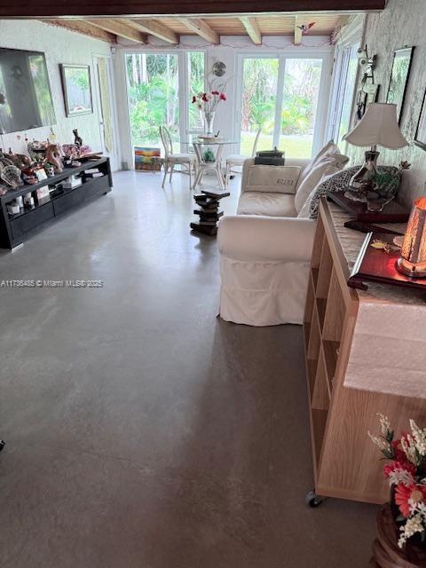 living area featuring beamed ceiling, plenty of natural light, and concrete floors