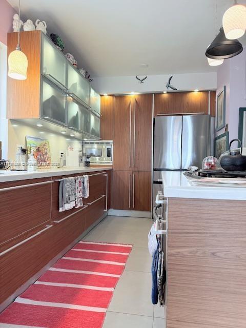 1643 Nethia Dr, Miami, FL 33133 - kitchen with light tile patterned flooring, light countertops, stainless steel appliances, pendant lighting, and brown cabinetry