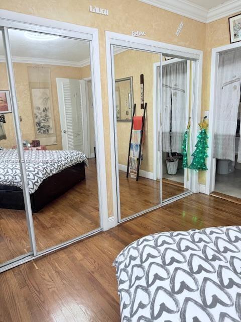 bedroom featuring wood finished floors, baseboards, two closets, and ornamental molding