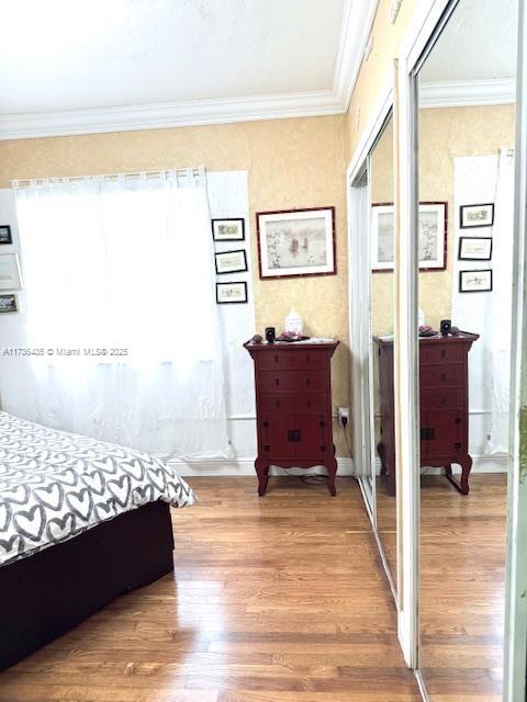 bedroom with a closet, wood finished floors, and crown molding