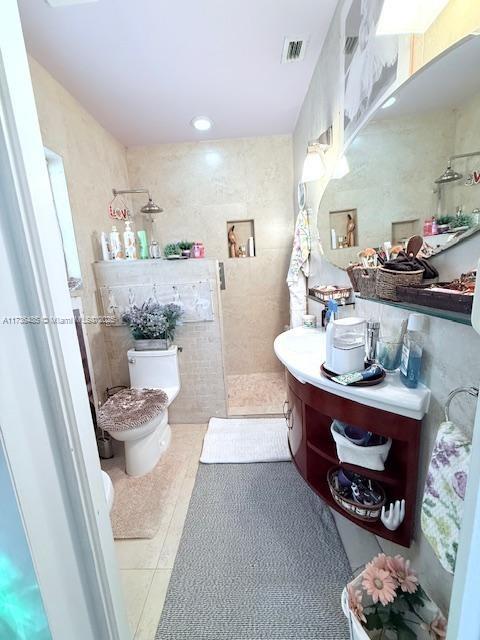 bathroom with vanity, tile patterned flooring, walk in shower, tile walls, and toilet