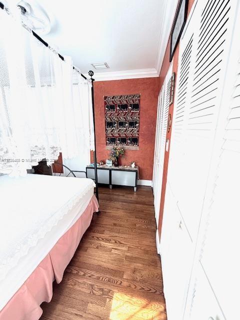 bedroom featuring baseboards, wood finished floors, visible vents, and ornamental molding