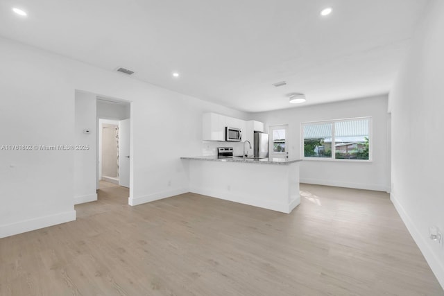 kitchen with light wood finished floors, visible vents, appliances with stainless steel finishes, a peninsula, and white cabinetry