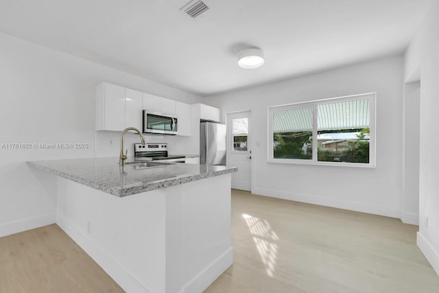 kitchen featuring a wealth of natural light, stainless steel appliances, a peninsula, and white cabinets