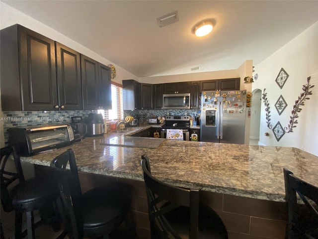 kitchen with backsplash, lofted ceiling, a kitchen breakfast bar, appliances with stainless steel finishes, and arched walkways