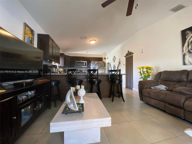 living room featuring vaulted ceiling, light tile patterned floors, a ceiling fan, and visible vents