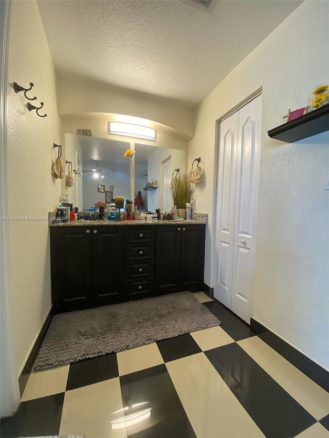 full bath with baseboards, double vanity, a textured wall, tile patterned floors, and a textured ceiling