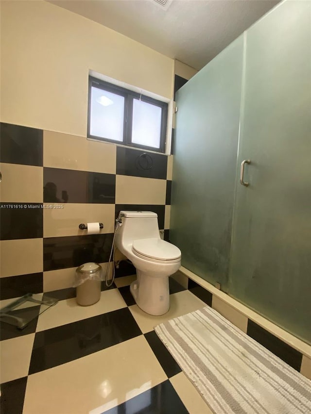 full bathroom with tile patterned floors, a stall shower, toilet, and tile walls