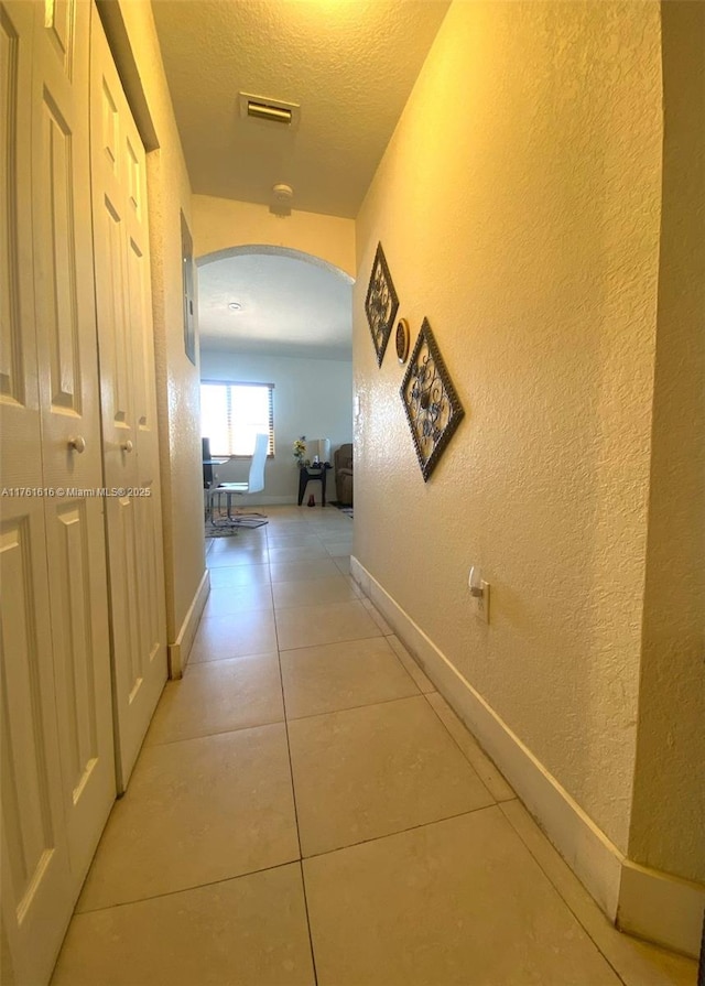 hall with light tile patterned floors, visible vents, arched walkways, a textured ceiling, and a textured wall